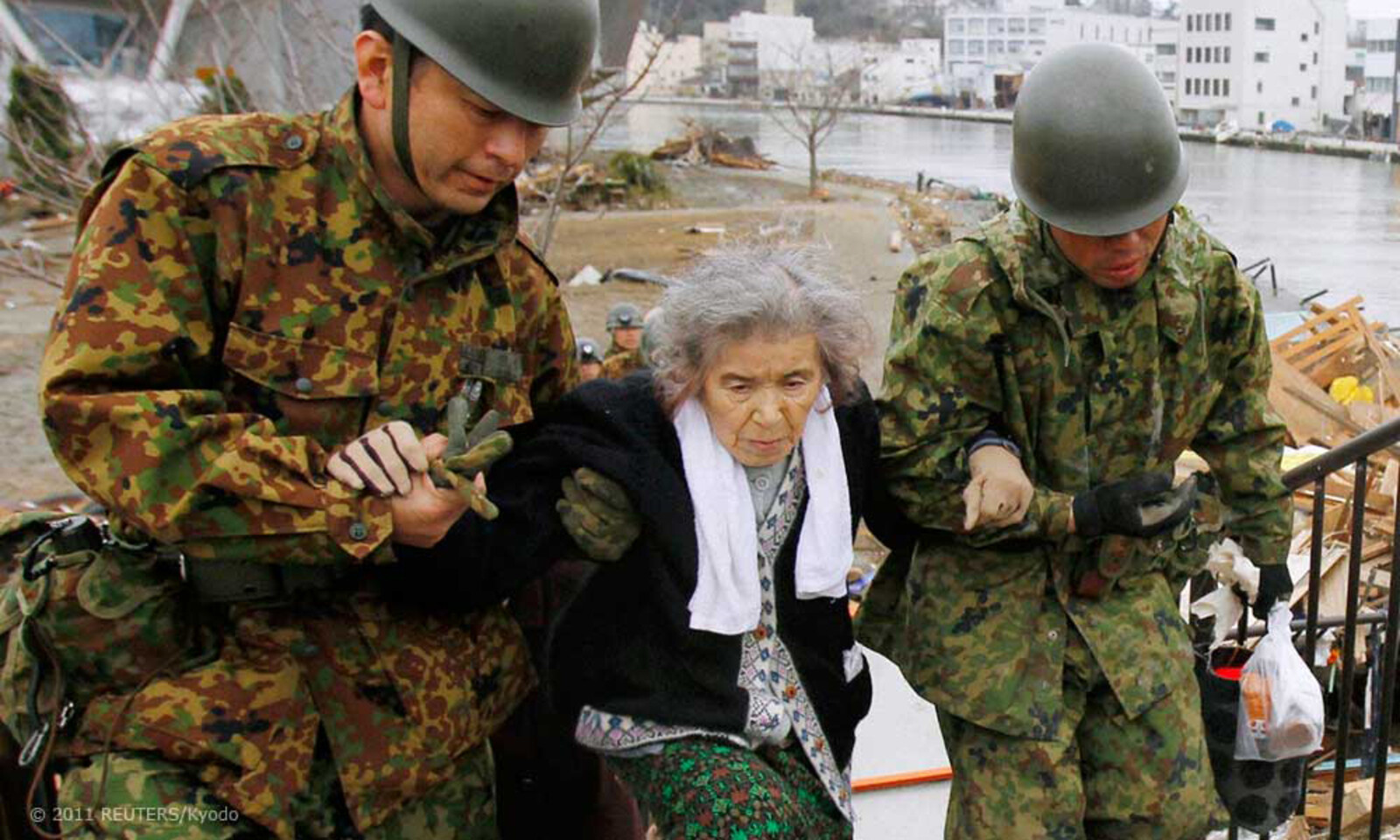 Soldaten bringen eine alte Frau in Sicherheit, die in einem von der Umwelt abgeschlossenen Rettungszentrum ausgeharrt hat.