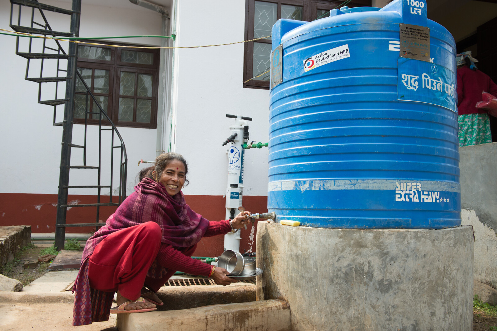 Eine Frau wäschst sich die Hände an einem neu errichteten Wassertank.