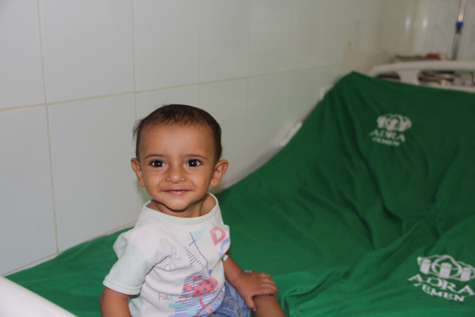 kleiner unterernährter Junge im Jemen sitzt auf einer grünen Decke mit dem Logo von ADRA