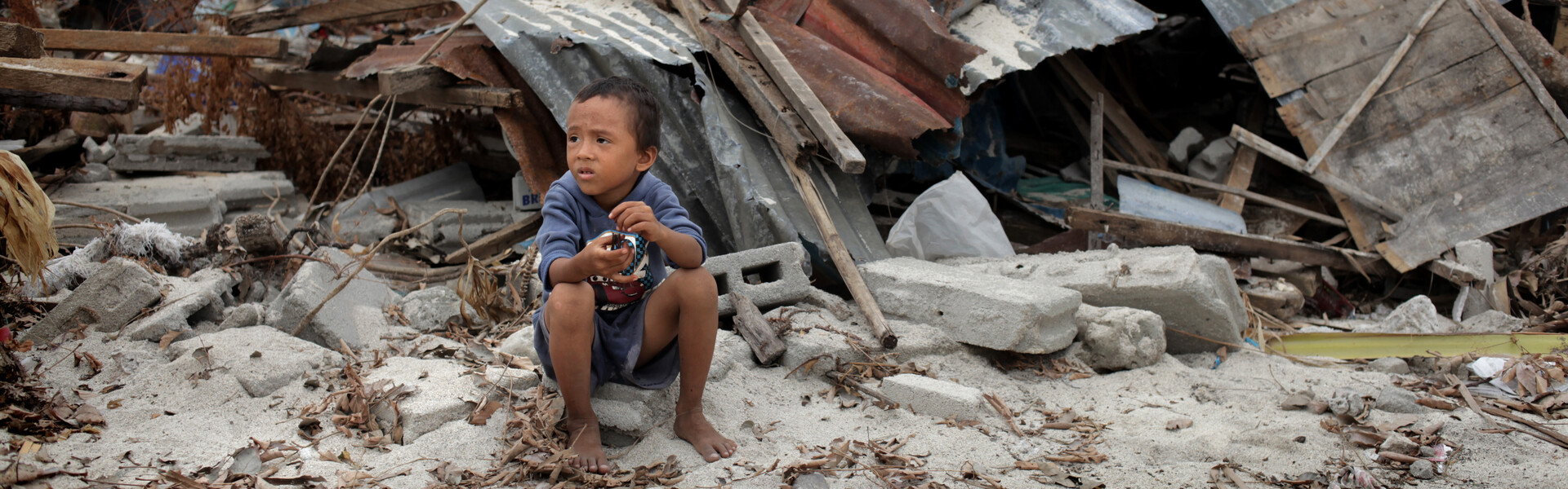 Kind sitzt vor einer Häuserruine auf den Philippinen nachdem Taifun Haiyan.