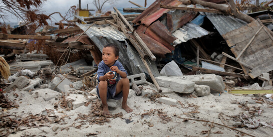 Kind sitzt vor einer Häuserruine auf den Philippinen nachdem Taifun Haiyan.