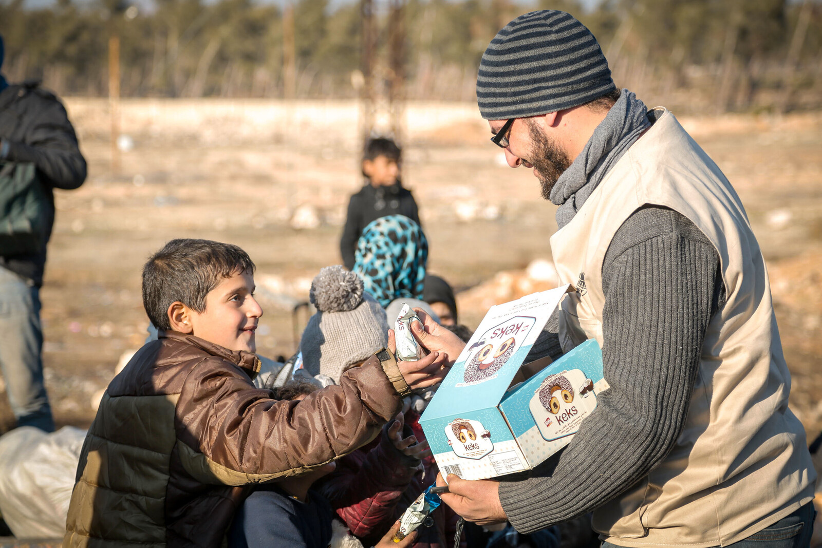 Ein Mitarbeiter einer Hilfsorganisation gibt einem syrischen Jungen einen Keks
