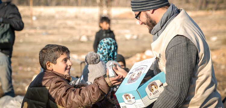 Ein Mitarbeiter einer Hilfsorganisation gibt einem syrischen Jungen einen Keks Ein Mitarbeiter einer Hilfsorganisation gibt einem syrischen Jungen einen Keks