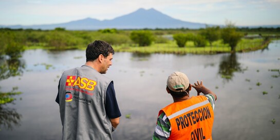 Zwei humanitäre Helfer vor einem überschwemmten Gebiet