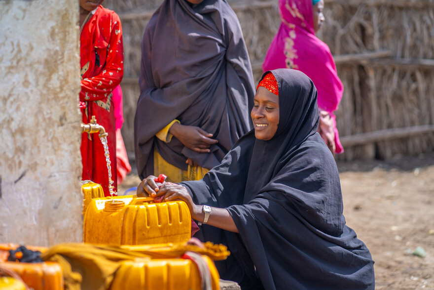Eine Frau füllt in Somalia an einer Wasserstelle Wasser in gelbe Kanister