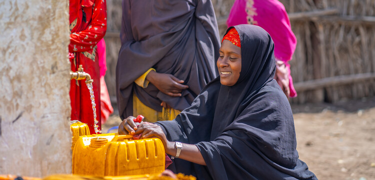 Eine Frau füllt in Somalia an einer Wasserstelle Wasser in gelbe Kanister