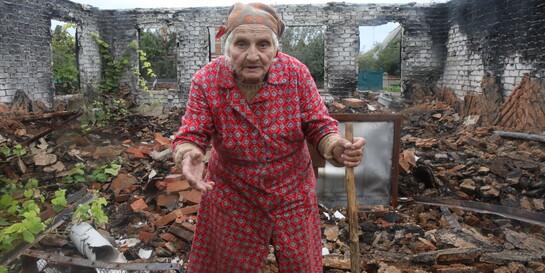 Eine alte Frau steht in der Ukraine in den Trümmern ihres Hauses