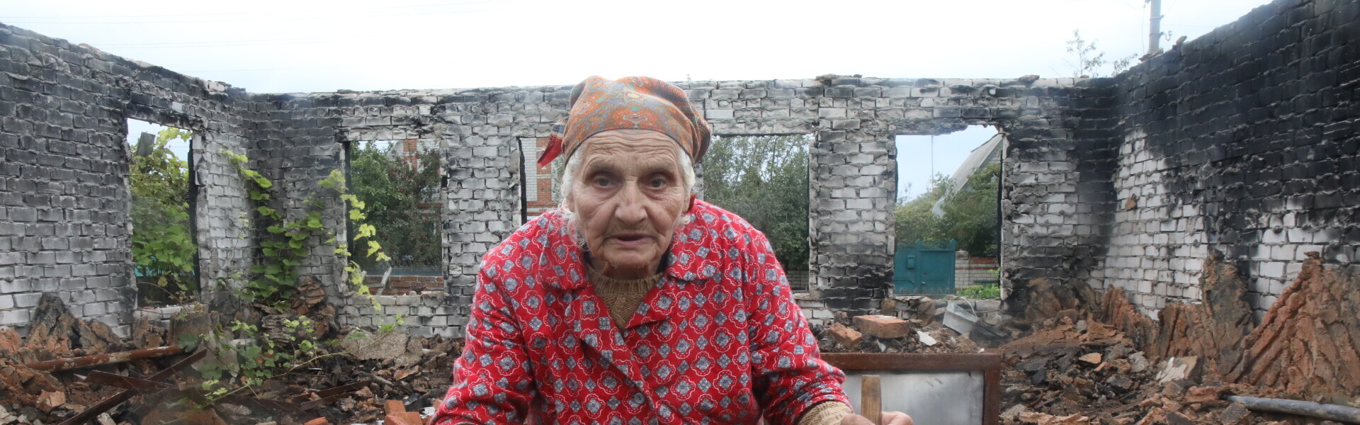 Eine alte Frau steht in der Ukraine in den Trümmern ihres Hauses