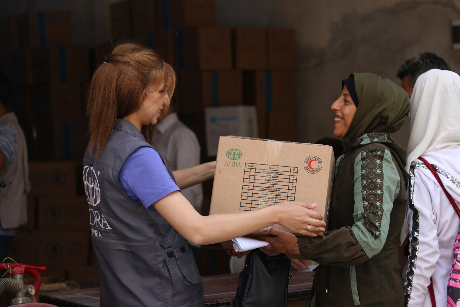 Eine Helferin übergibt einer Frau ein Paket mit Hygieneprodukten