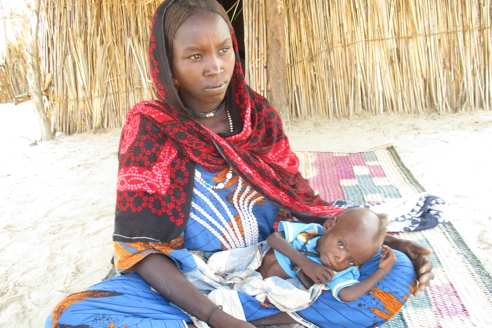 Eine Frau im Tschad sitzt mit ihrem Baby auf dem Boden. Sie wartet auf Nothilfe.