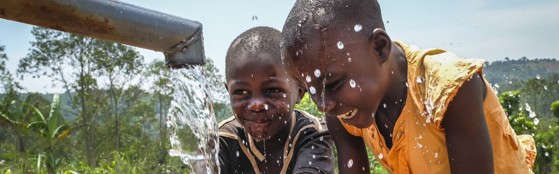 Kinder in Uganda spielen an einem Brunnen mit Wasser