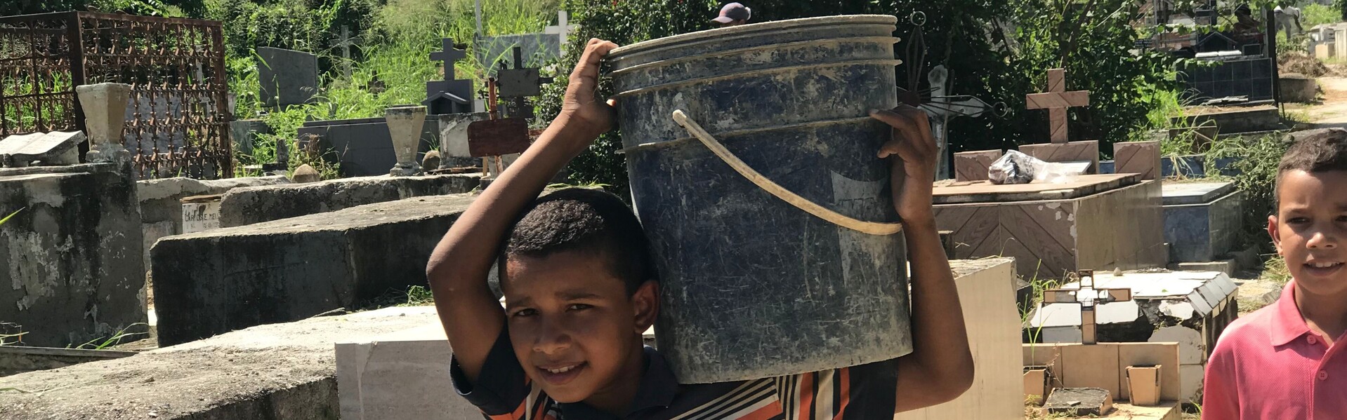 Ein Junge in Venezuela trägt auf einem Friedhof einen Eimer auf der Schulter