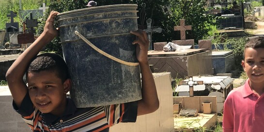 Ein Junge in Venezuela trägt auf einem Friedhof einen Eimer auf der Schulter