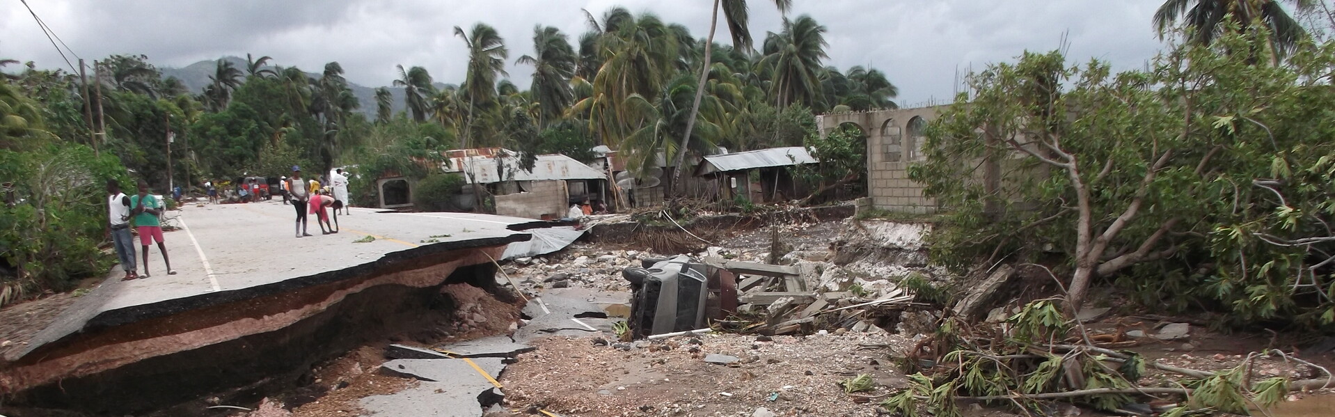 Menschen stehen vor einer durch Hurrikan Matthew zerstörten Straße auf Haiti.