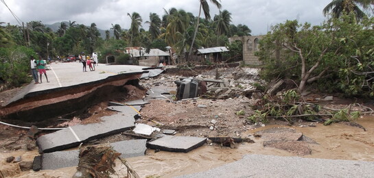 Menschen stehen vor einer durch Hurrikan Matthew zerstörten Straße auf Haiti.
