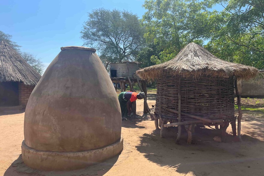 Ein neue neben einem alten Getreidespeicher in Sambia, dahinter eine Frau
