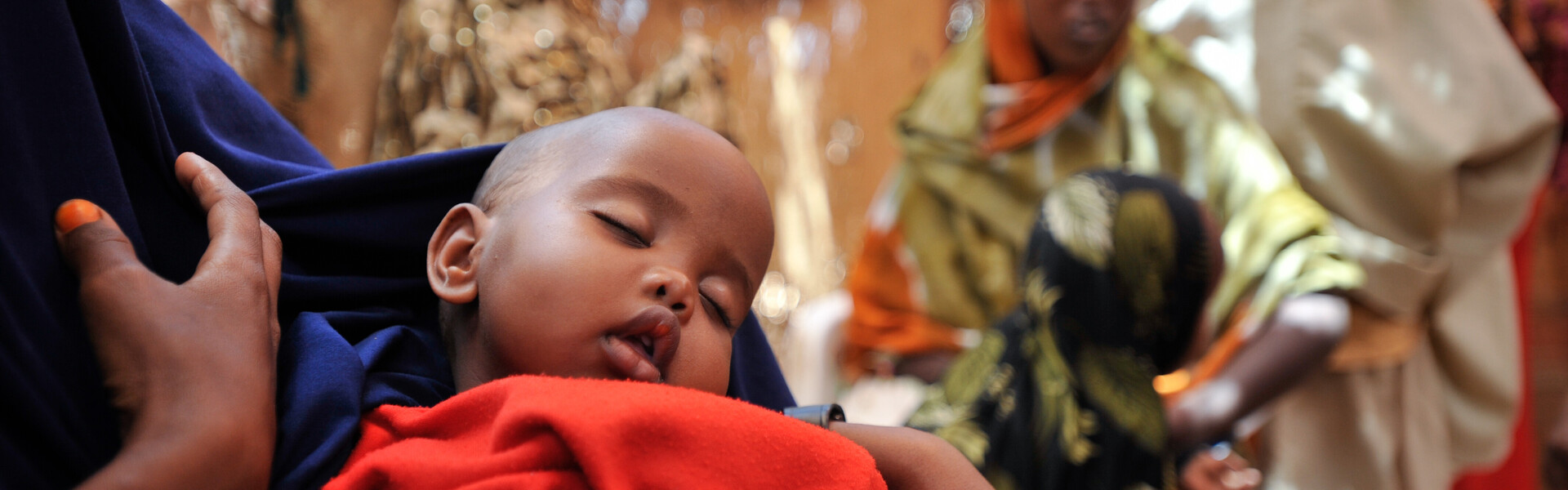 Ein kleines Kind schläft auf dem Arm seiner Mutter in einem Flüchtlingszelt an der Grenze zu Somalia. Vor Kriegen und Gewalt fliehen dort immer mehr Menschen.