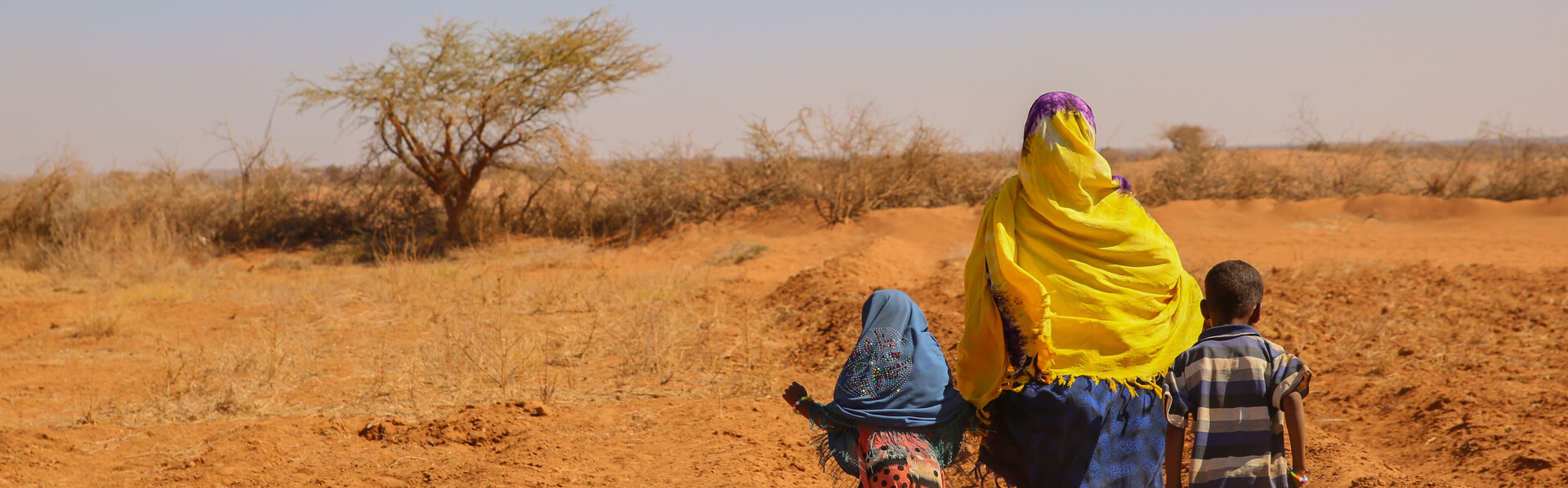 Eine Frau mit Kopftuch spaziert mit ihren zwei Kindern über ein ausgetrocknetes Feld in Somalia