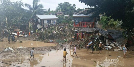 Menschen stehen auf den Philippinen vor zerstörten Häusern und auf überfluteten Straßen