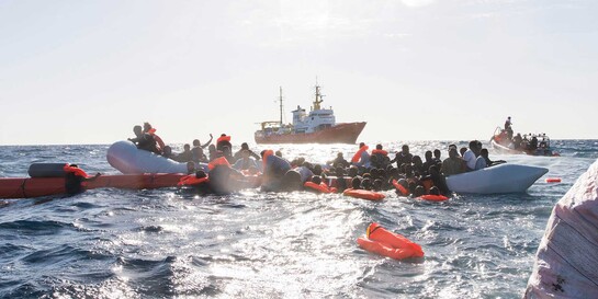 Menschen sind auf einem Schlauchboot im Mittelmeer und werden aus ihrer Seenot gerettet
