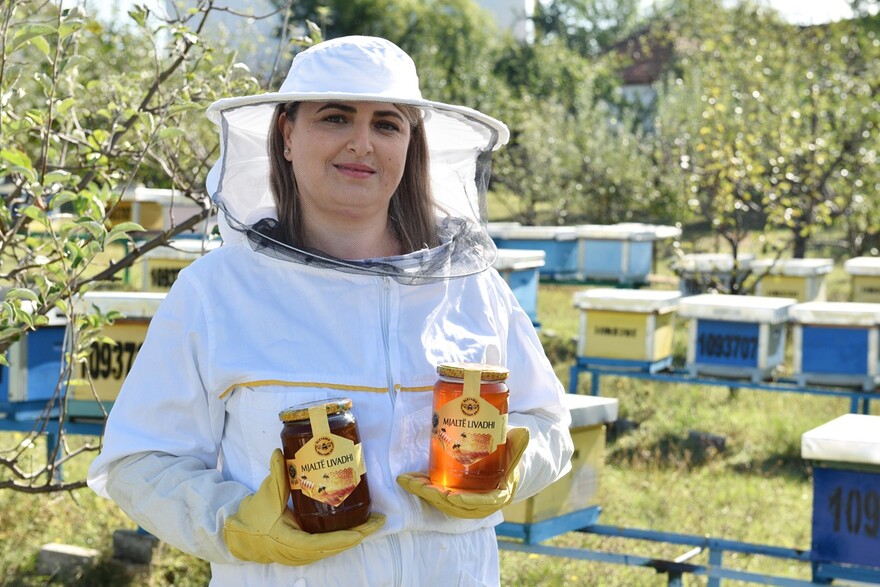 Eine Imkerin hält zwei Honiggläser in der Hand und lächelt in die Kamera