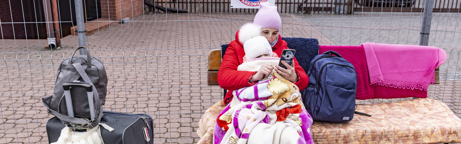 Eine aus der Ukraine geflüchtete Frau sitzt mit ihrem Baby auf dem Arm auf einer mit Decken überworfenen Holzbank