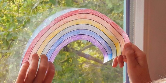 Hoffnung während Corona: Ein Kind hängt einen Regenbogen ins Fenster