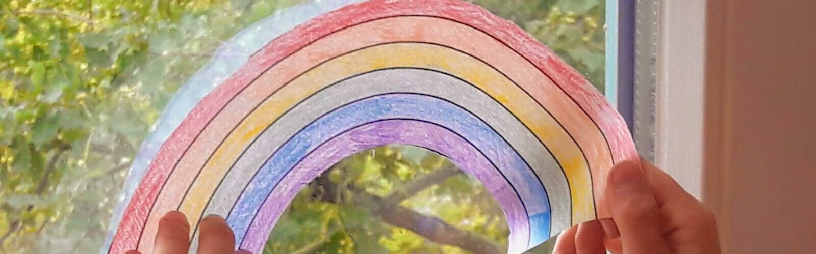 Hoffnung während Corona: Ein Kind hängt einen Regenbogen ins Fenster
