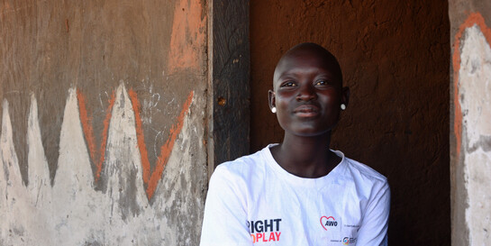 Eine Helferin von der Hilfsorganisation AWO International sitzt vor einem Haus in Uganda und lächelt in die Kamera