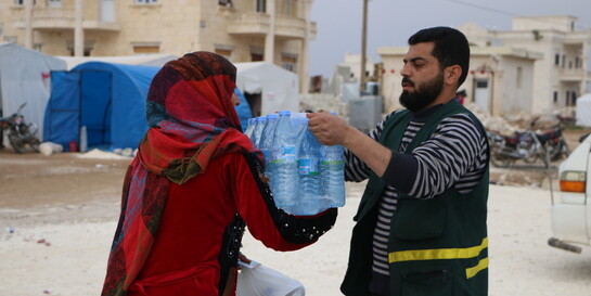 Helfer übergibt Frau in syrischem Erdbebengebiet Trinkwasser