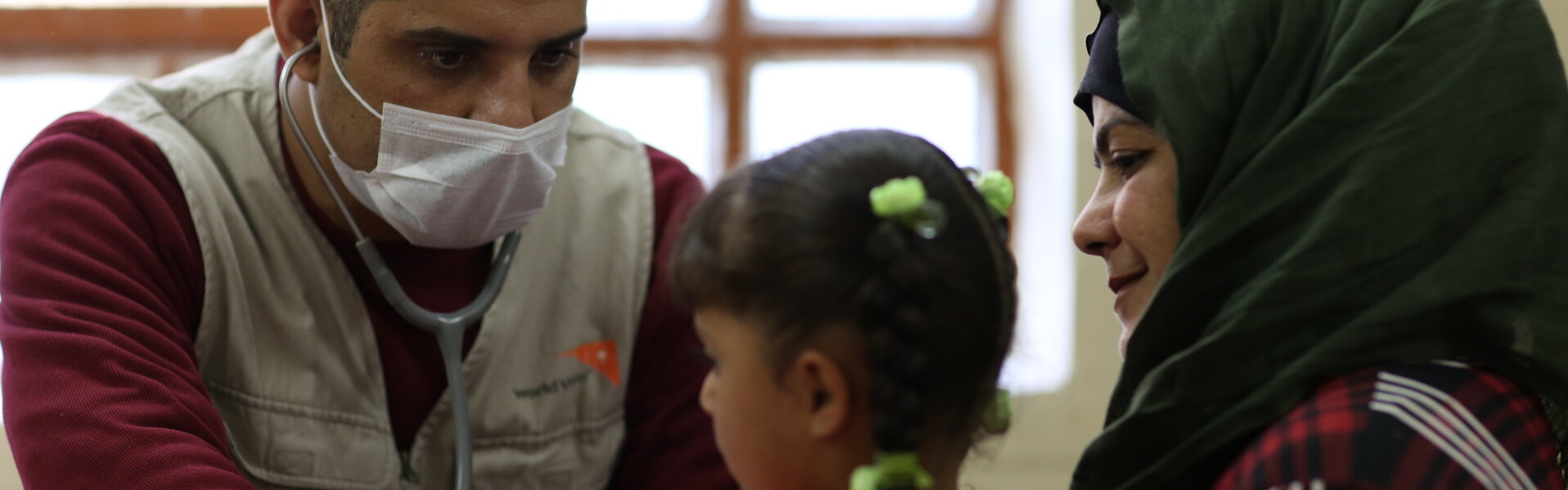 Ein Arzt untersucht ein Kind im Beisein der Mutter mit einem Stethoskop