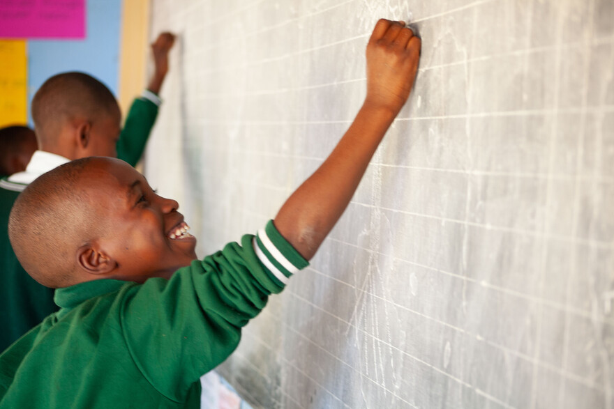 Zwei jungen stehen in einer Schule in Simbabwe an der Tafel und schreiben mit Kreide darauf
