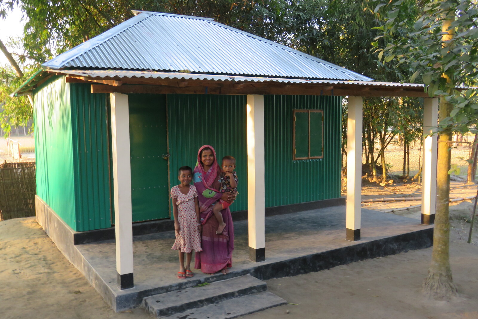 Eine Frau steht mit ihren zwei Kindern auf der Veranda ihrer grünen Blechhütte