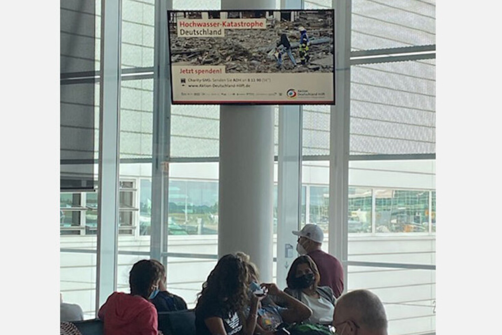 Cittadino schaltet im Boardingbereich eines Flughafens Werbung für Aktion Deutschland Hilft