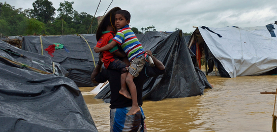Ein Junge auf dem Arm seines Vaters in einem der überschwemmten Flüchtlingscamps in Bangladesch