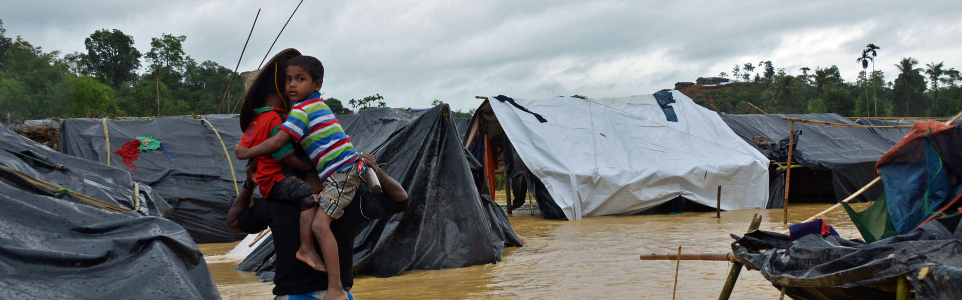 Ein Junge auf dem Arm seines Vaters in einem der überschwemmten Flüchtlingscamps in Bangladesch