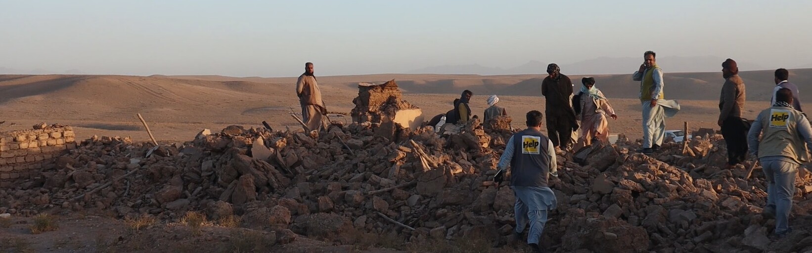 Menschen nach einem Erdbeben in Afghanistan inmitten von Trümmern, begleitet von einem Helfer (Symbolbild)