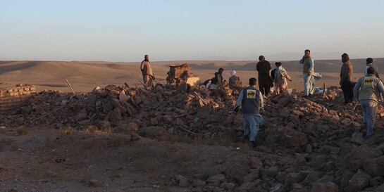 Menschen nach einem Erdbeben in Afghanistan inmitten von Trümmern, begleitet von einem Helfer (Symbolbild)