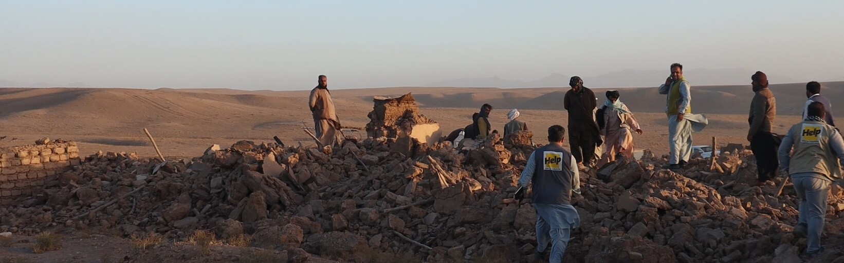 Menschen nach einem Erdbeben in Afghanistan inmitten von Trümmern, begleitet von einem Helfer (Symbolbild)