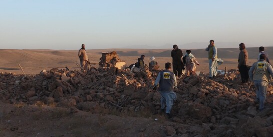 Menschen nach einem Erdbeben inmitten von Trümmern, begleitet von einem Helfer (Symbolbild)