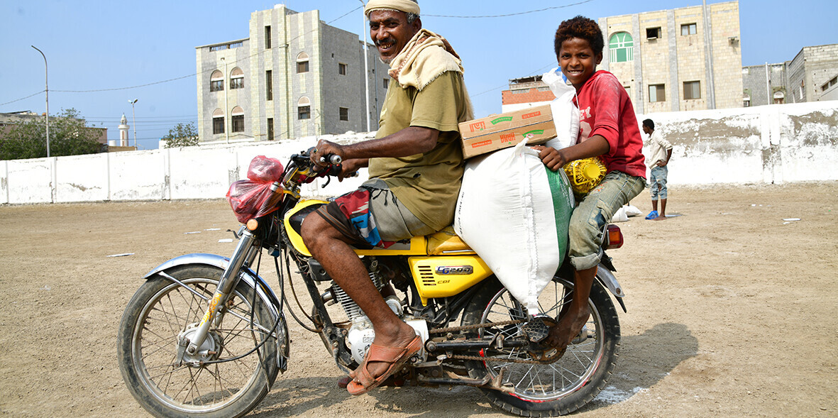 Vater und Sohn transportieren mit dem Moped das Lebensmittelpaket, das sie von der Organisation LandsAid erhalten haben Vater und Sohn transportieren mit dem Moped das Lebensmittelpaket, das sie von der Organisation LandsAid erhalten haben