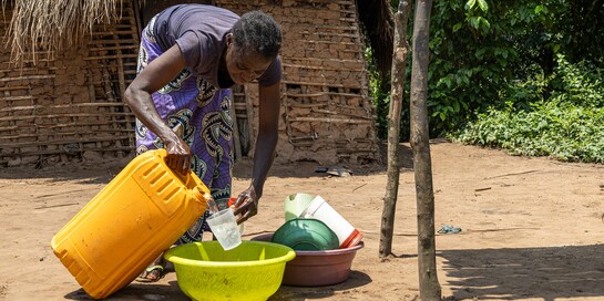Eine Frau füllt Wasser aus einem großen Behälter in einen kleinen Becher