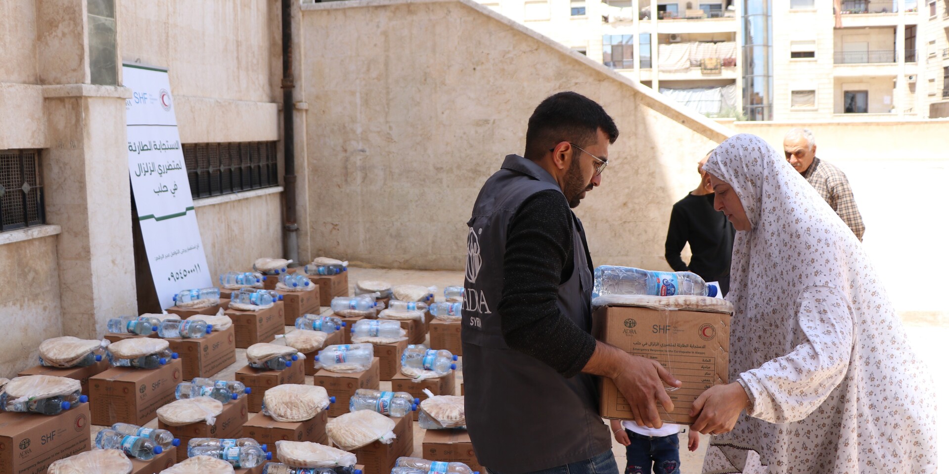 Ein Helfer von ADRA überreicht einer Frau in Syrien Wasser und ein Lebensmittelpaket