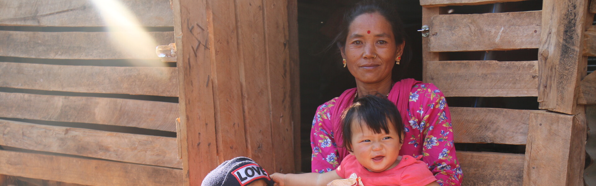 In Nepal sitzt eine Frau  mit ihren Kindern vor einer Hütte - zwei Jahre nach dem Erdbeben