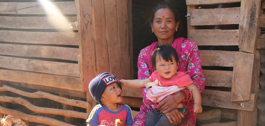 In Nepal sitzt eine Frau  mit ihren Kindern vor einer Hütte - zwei Jahre nach dem Erdbeben