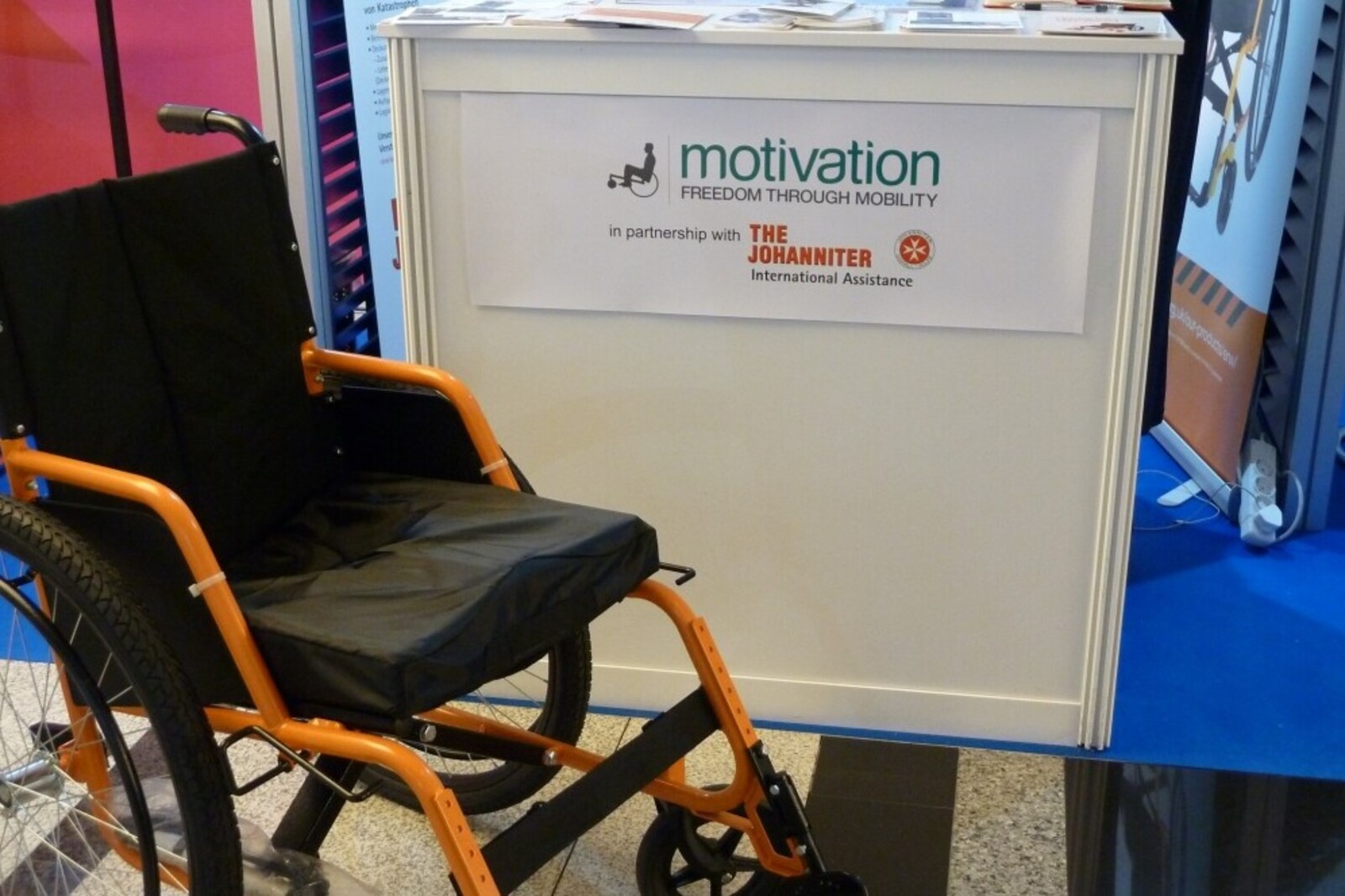 Ein Rollstuhl steht vor einem Pult der Johanniter in der Ausstellungshalle des Worlds Humanitarian Summit.