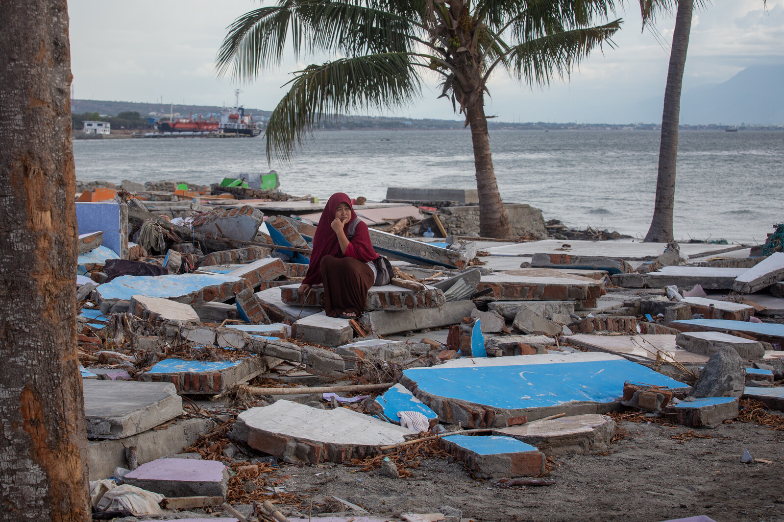 Eine Frau in Indonesien sitzt verzweifelt an einem Strand umgeben von Trümmern, nachdem das Erdbeben in Sulawesi einen Tsunami auslöste