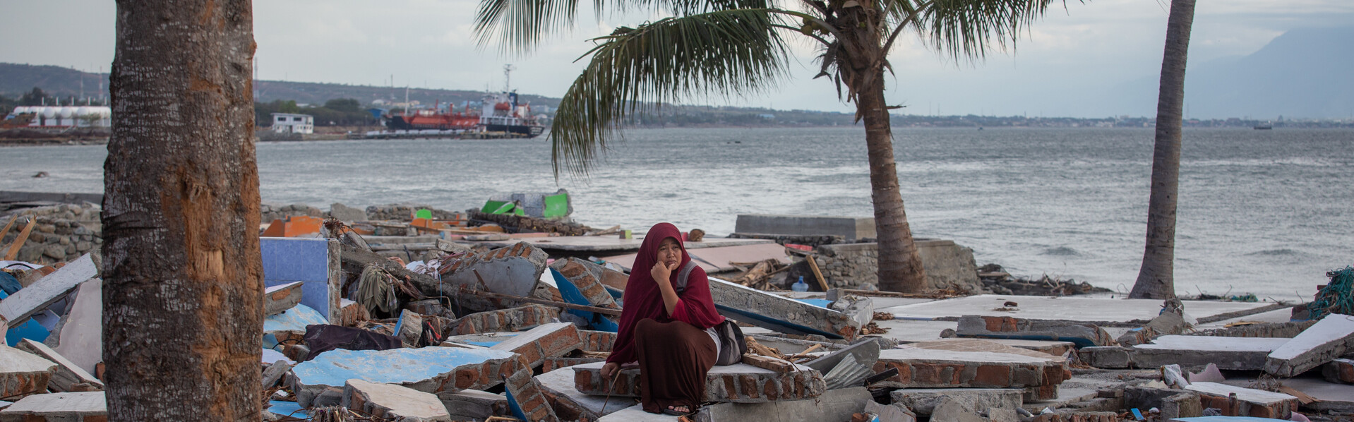 Eine Frau in Indonesien sitzt verzweifelt an einem Strand umgeben von Trümmern, nachdem das Erdbeben in Sulawesi einen Tsunami auslöste