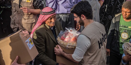 Ein Helfer in Syrien gibt einem älteren Mann Lebensmittel