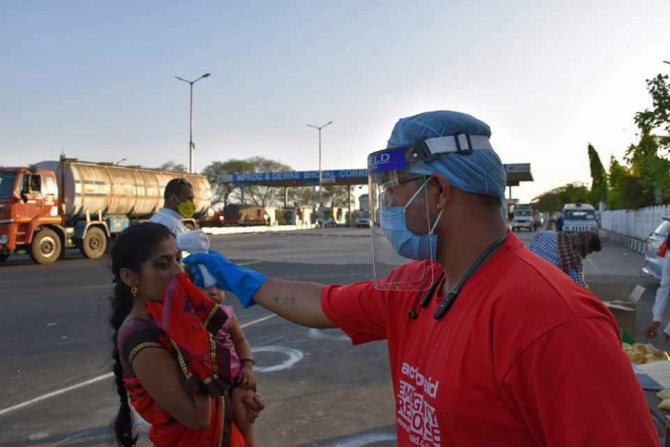 Ein Helfer misst Fieber bei einer Frau in Indien